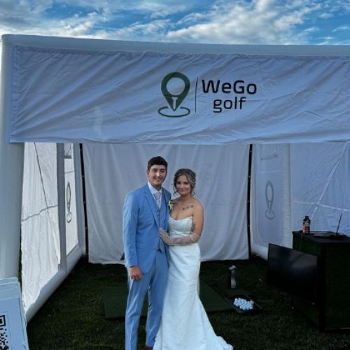 Bride in a white wedding gown and a groom in a light blue suit pose inside a white canopy with a WeGo golf logo backdrop.
